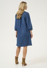 Jeansjurk met een relaxed fit, knielang, met pofmouwen, subtiele stikseldetails en een effen blauwe kleur. Gemaakt in combinatie met tan enkelboots.