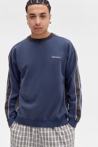 Mørkeblå genser med ribbestrikket krage, hvite sidestriper og logo-patch på brystet; myk tekstur, oversized passform.