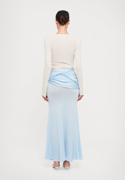 Saia drapeada azul claro com um top ajustado de manga longa em creme. Textura de tecido suave; detalhe de design ajustado na cintura.