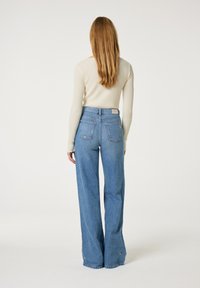 Lichtblauwe, hooggewaiste, wijde jeans met een vervaagd textuur. Bevat twee achterzakken en een klein logo-patch.
