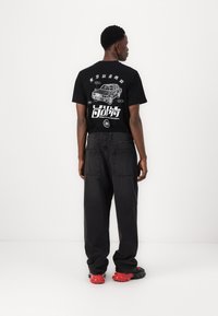 Black t-shirt with graphic print of a car and text on the back, paired with loose dark jeans and red-and-black sneakers.