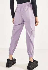 Jasnofioletowe spodnie cargo z elastycznym pasem, bocznymi kieszeniami i elastycznymi mankietami, w połączeniu z czarnymi trampkami na platformie.