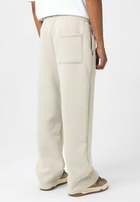 Lichtbeige sweatpants van zacht materiaal, met een achterzak, relaxed fit en een verstelbare tailleband. Gecombineerd met bruine sneakers.