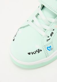 Menta zöld sportcipők sima textúrával, játékos grafikákkal, beleértve a "KISS" és "NO" feliratokat, valamint csillag és szív mintákat.