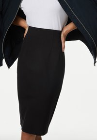 Schwarzer Bleistiftrock aus glattem, dehnbarem Stoff; knielanges Design mit vorderen Falten und tailliertem Schnitt. Kombiniert mit einem weißen T-Shirt.