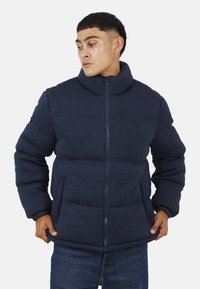 Granatowa kurtka puchowa z fakturowanej tkaniny, z wysokim kołnierzem, zapięciem na zamek błyskawiczny i dwiema przednimi kieszeniami.