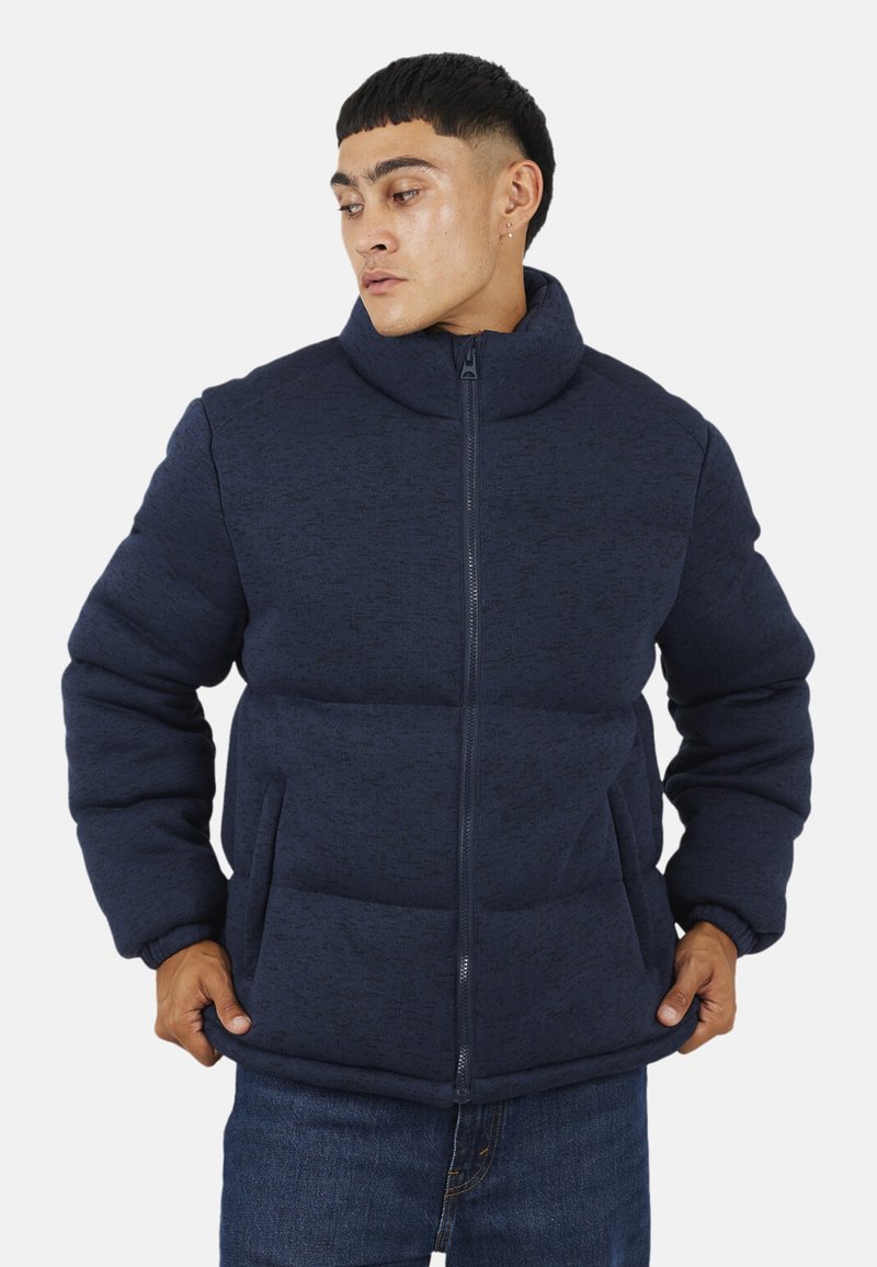 Granatowa kurtka puchowa z fakturowanej tkaniny, z wysokim kołnierzem, zapięciem na zamek błyskawiczny i dwiema przednimi kieszeniami.