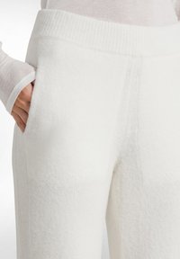 Witte gebreide broeken met een zachte textuur, brede geribbelde tailleband en zijzakken. Naaddetails zijn zichtbaar langs de benen.