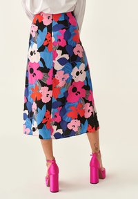 Falda midi con estampado floral en colores vibrantes de rosa, azul y negro. Presenta un corte recto y una textura suave, combinada con sandalias de tacón bloque en rosa.