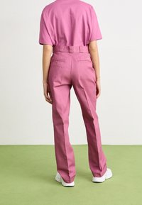 Roze stoffen broek met een rechte pijp, hoge taille en achterzakken. Gecombineerd met een bijpassend topje met korte mouwen en witte schoenen.
