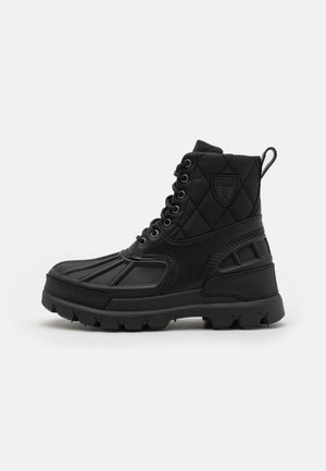 Botte noire montante avec cheville en tissu matelassé, semelle robuste, laçage à l'avant et écusson Polo sur le côté.