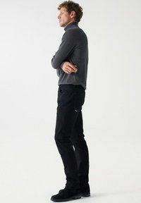 Crne traperice uskog kroja, uparene s tamno sivim dolčevitom. Tkanina izgleda glatko, a silueta je uska.