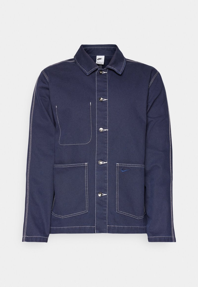 Chaqueta azul marino confeccionada en material similar al denim, con cierre de botones, dos bolsillos frontales, costuras blancas y un pequeño logo.