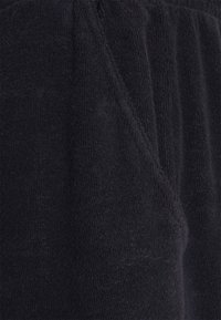 Schwarzterrierstoff mit weicher Textur, der feine vertikale Linien aufweist. Das Kleidungsstück hat eine lockere Passform und Taschen an den Seiten.