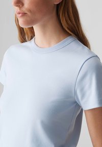 Hellblaues Baumwoll-T-Shirt mit kurzen Ärmeln und geripptem Rundhalsausschnitt, das über eine glatte Textur und eine taillierte Passform verfügt.