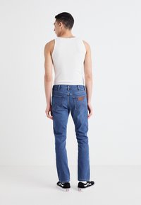 Niebieskie dżinsy o prostym kroju, z subtelnym przeszyciem, brązową skórzaną łatą z tyłu i czarnymi trampkami.