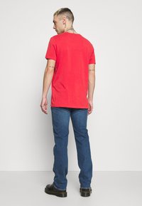 Rode t-shirt met korte mouwen en ronde hals, gemaakt van katoen. Het model draagt blauwe spijkerbroeken en zwarte laarzen, gezien vanuit de achterkant.