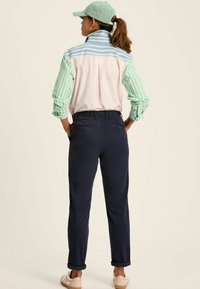 Koszula z kołnierzykiem w multikolorowy pasek, z zielonymi i białymi rękawami; granatowe spodnie z elastycznym paskiem i podwiniętymi nogawkami; beżowe buty.