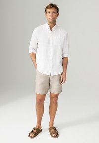 Weißes Leinenhemd mit Knöpfen und hochgekrempelten Ärmeln, beige Shorts und braune Sandalen mit offenen Zehen. Keine bemerkenswerten Muster oder Akzentuierungen.
