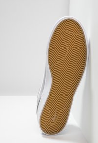 Weißer Sneaker mit Gummisohle; strukturiertes Fischgrätenmuster in Braun; Obermaterial aus Wildleder; minimales Branding sichtbar an der Seite.