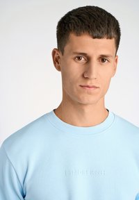 Ljusblå sweatshirt med rundad halsringning, prydd med präglat varumärkesnamn "LINDBERGH" på framsidan. Mjuk tygkvalitet och avslappnad passform.