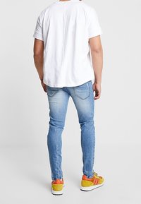 Camiseta blanca de manga corta, jeans ajustados de color azul claro y zapatillas multicolores con acentos en amarillo, naranja y blanco.