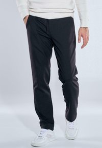 Black trousers with a relaxed fit, featuring an adjustable drawstring waist and smooth texture. Paired with white sneakers.