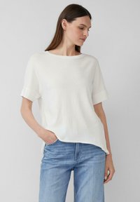 Witte korte mouwen top met een ronde halslijn en omgeslagen mouwen. Zachte textuur en relaxte pasvorm, gecombineerd met lichtblauwe denim jeans.