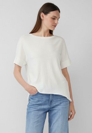 Witte korte mouwen top met een ronde halslijn en omgeslagen mouwen. Zachte textuur en relaxte pasvorm, gecombineerd met lichtblauwe denim jeans.