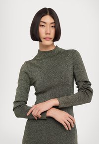 Figurnära, långärmad klänning i mörkgrön med metallisk glans. Hög krage och mjuk textur. Subtil ribbning på ärmarna.