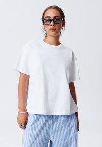 T-shirt en coton blanc avec une coupe décontractée, des manches courtes et un col ras du cou, associé à un pantalon à rayures bleues.