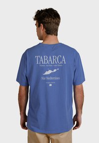 Blaues Baumwoll-T-Shirt mit einem bedruckten Design auf der Rückseite, das "TABARCA" und eine Karte von der Insel Tabarca in weißem Text enthält.