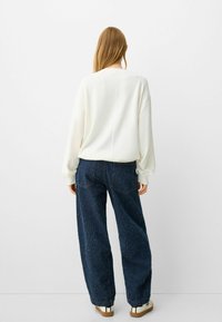 Przewymiarowany biały sweter z prążkowanymi mankietami w połączeniu z luźnymi, ciemnoniebieskimi dżinsami z tylnymi kieszeniami i teksturowanym wykończeniem.