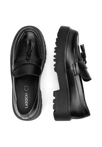 Černé kožené mokasíny s akcentem v podobě třásní, zaobleným tvarem a silnou gumovou podrážkou s texturovaným vzorem. Vnitřek má branding.