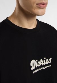 Black cotton t-shirt with a crew neck, featuring white embroidered text "Dickies WORKWEAR COMPANY" on the left chest area.