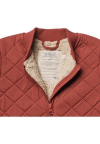 Rustfarvet quiltet jakke med cremefarvet fleeceforing og krave, delvist åbnet for at afsløre et "WHEAT" mærke inde i jakken.