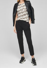 Pantaloni neri su misura abbinati a un top senza maniche a fantasia con tonalità di bianco, marrone e nero. Una giacca in pelle nera attillata completa l'outfit.