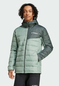 Chaqueta acolchada verde con un diseño texturizado, que presenta un cierre frontal con cremallera, capucha ajustable y detalles en un verde oscuro contrastante. Logo "TERREX" visible.