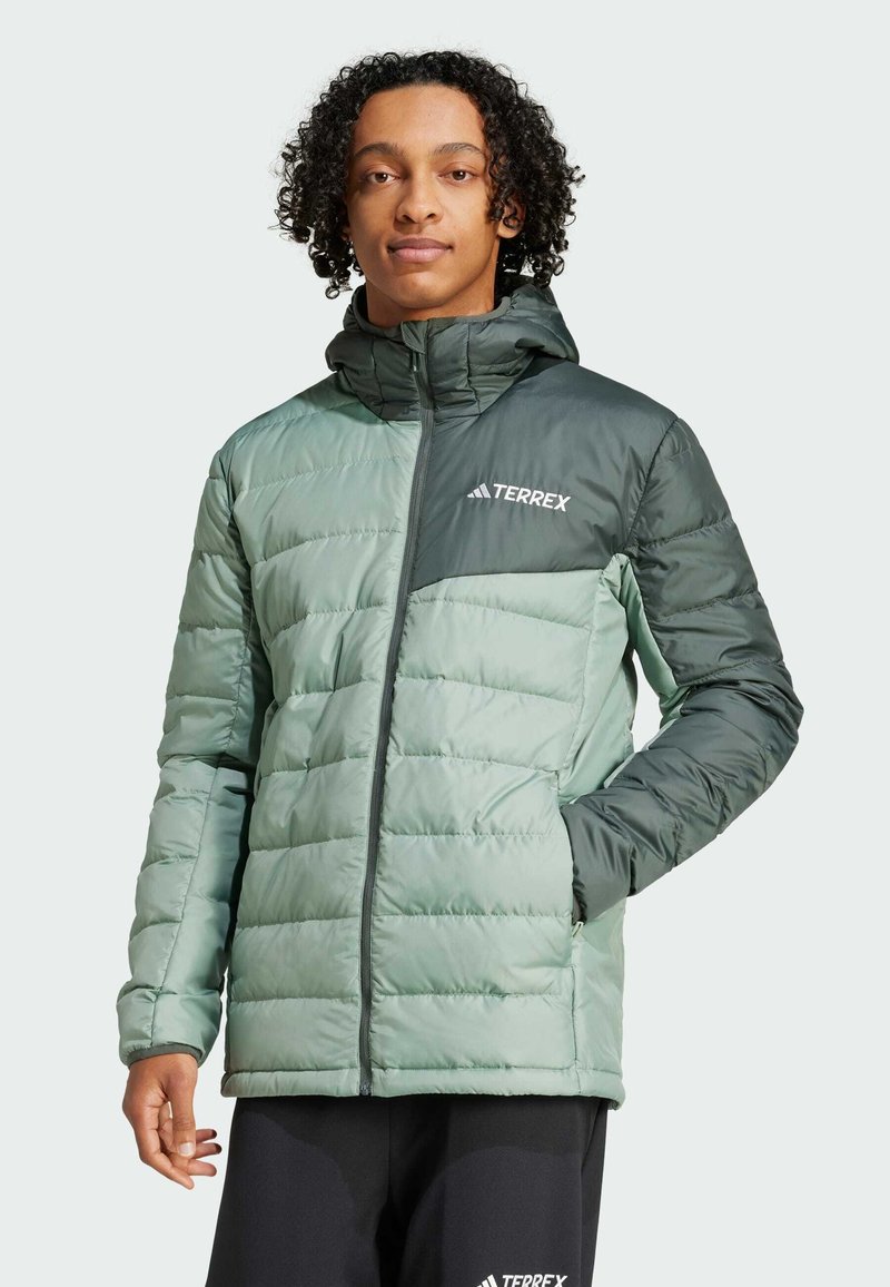 Chaqueta acolchada verde con un diseño texturizado, que presenta un cierre frontal con cremallera, capucha ajustable y detalles en un verde oscuro contrastante. Logo "TERREX" visible.