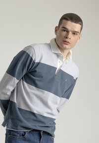 Camisa polo de manga larga con rayas horizontales en gris y azul marino, con un cuello blanco y una tapeta con botones. Material de algodón suave.
