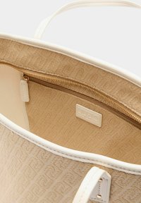Beige katoenen draagtas met crème afwerking, voorzien van een ritspocket aan de binnenkant, een gestructureerd patroon, een logolabel en gladde, leerachtige handvatten.