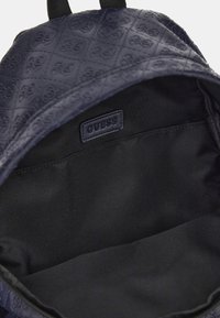 Zaino blu navy con motivo impresso, chiusura con zip e interno in tessuto nero con etichetta di marca. Forma semplice e strutturata.