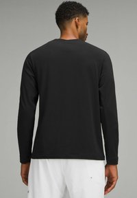 Tricou negru cu mânecă lungă, guler rotund, textură netedă și croială ajustată. Stil minimalism, fără logo-uri sau modele vizibile.