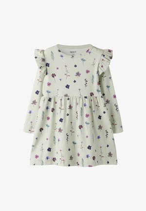 Vestido de manga larga color crema con estampado floral en tonos púrpura y rosa, con detalles de volantes en los hombros y cintura fruncida.