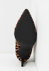 Chaussure à talon haut avec bout pointu, semelle noire et dessus imprimé animal marron et noir, vue du dessous sur fond blanc.