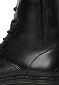 Melna ādas potīšu zābaki ar gludu apdari, ar auklām savelkamu dizainu, sānu rāvējslēdzēju un teksturētu zoli ar trīsstūra rakstu.