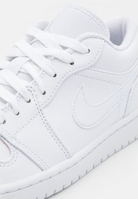 Gros plan d'une sneaker en cuir blanc avec des lacets blancs, des détails de couture et un logo swoosh cousu sur le côté.