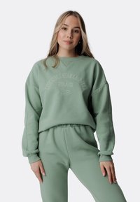 Felpa verde menta con colletto a giro e testo ricamato "Le ragazze cool indossano Laurella Polonia 2018". Presenta spalle scese e polsini a coste.