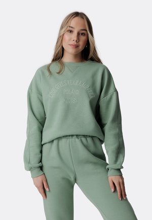 Mentolovo zelený mikinový sveter s okrúhlym výstrihom a vyšitým textom "Cool Girls Wear Laurella Poland 2018." Obsahuje spadnuté ramená a rebrované manžety.