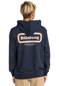 Sudadera con capucha color navy que presenta un logo de "Billabong" en blanco y naranja en la parte trasera, con textura suave y puños y dobladillo acanalados.